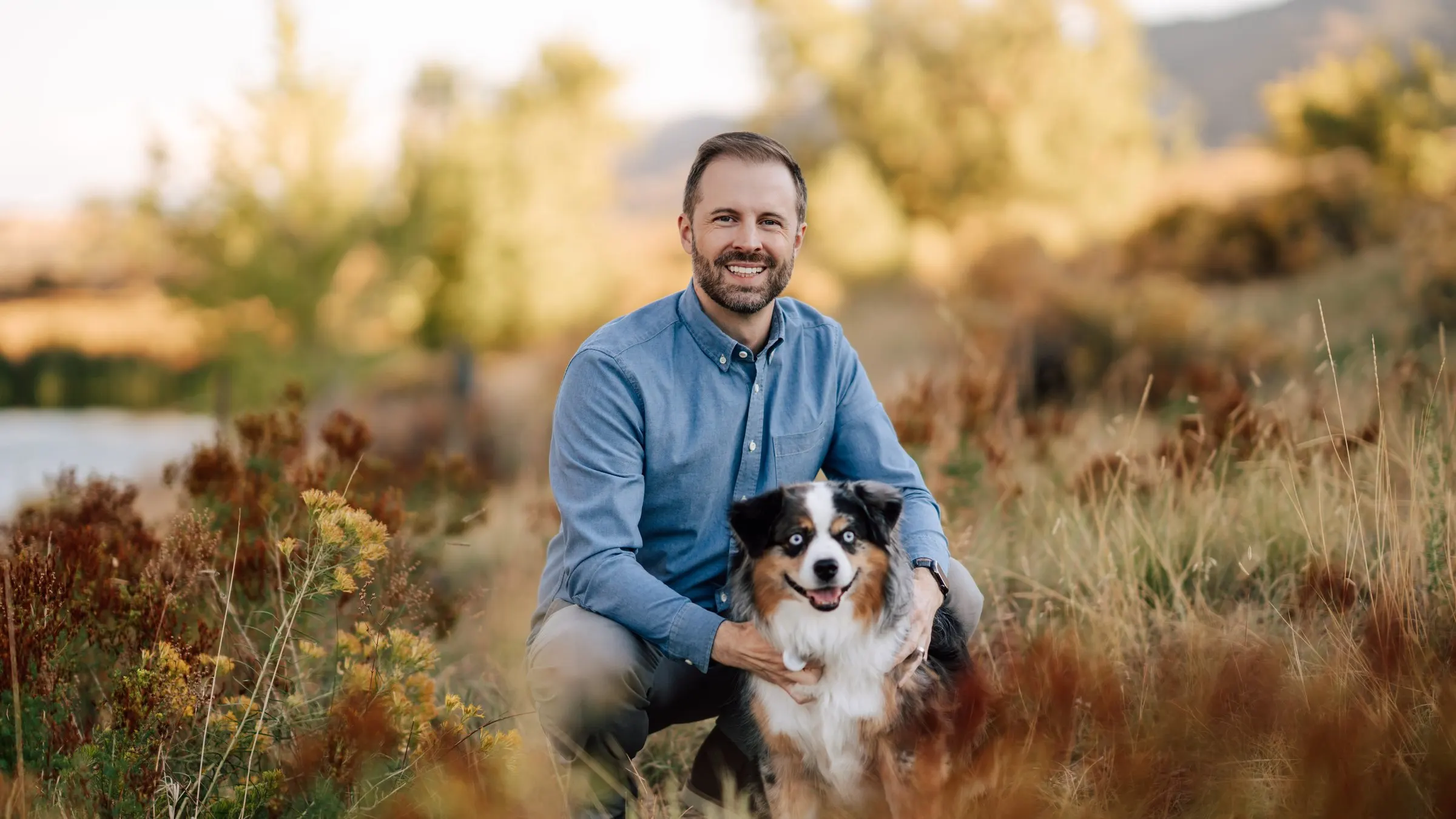 Tyler Marshall, MA, LPCC, crouching with his dog in the Colorado foothills