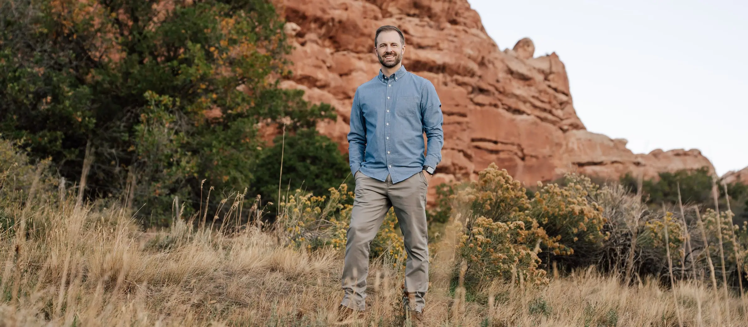 Tyler Marshall standing in tall grass below a red rock cliff
